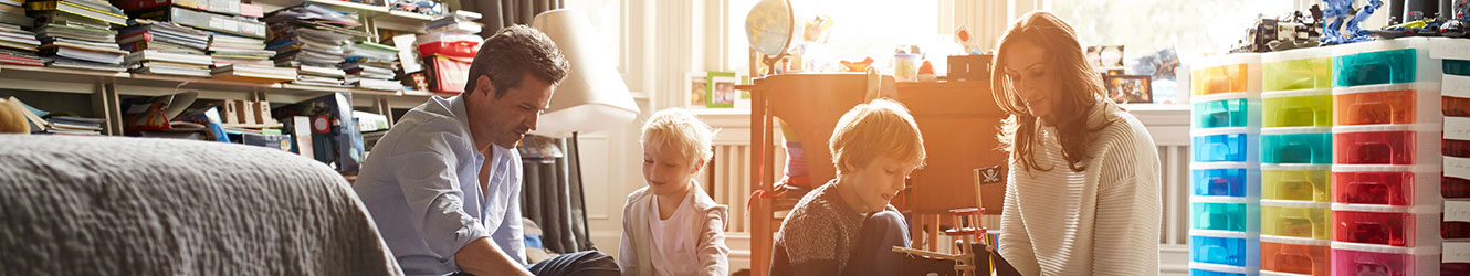 Parents with 2 sons playing with toys in their room.