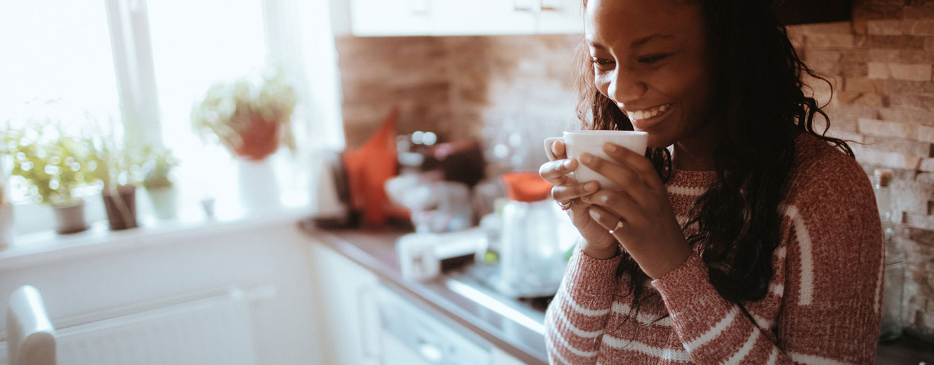 Woman in kitchen sipping coffee.
